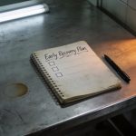 Open notebook on a scratched metal table with ‘Early Recovery Plan’ written at the top for the Early Recovery Guide.
